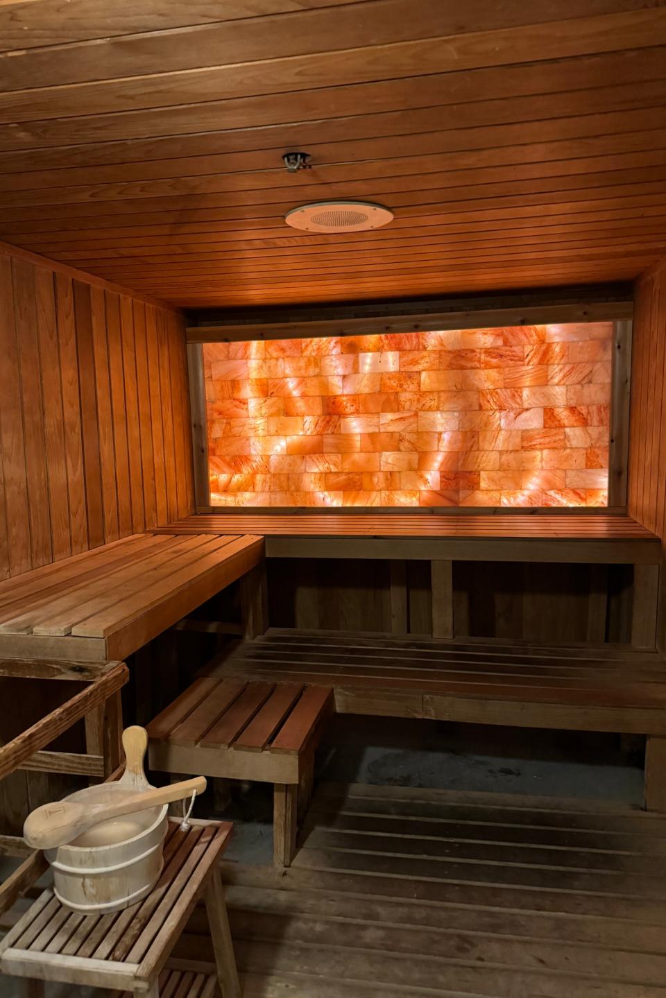 A wooden sauna with benches and a large salt wall, including a ladle and bucket