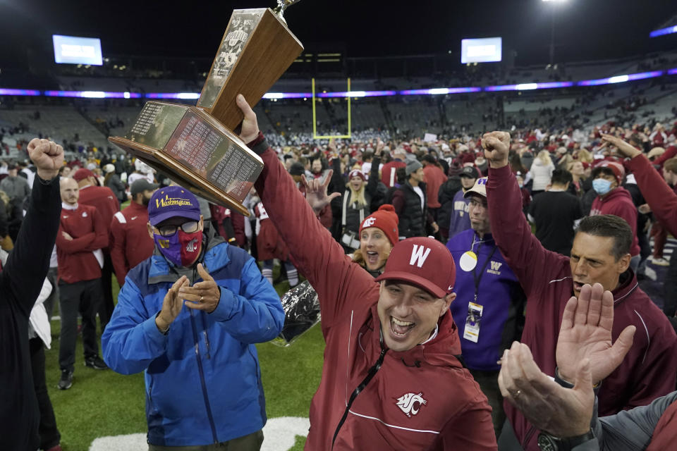 Washington State acting head coach Jake Dickert, center, holds up the Apple Cup Trophy after it was presented to him by Washington Gov. Jay Inslee, left, after Washington State beat Washington 40-13 in an NCAA college football game, Friday, Nov. 26, 2021, in Seattle. (AP Photo/Ted S. Warren)