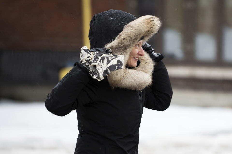 A woman braces strong winds as she crosses a street in The Glebe neighborhood of Ottawa, on Friday, Dec. 23, 2022. Environment Canada has issued a winter storm warning for the region which is calling for flash freezing, icy and slippery surfaces, wind gusts and chills. (Spencer Colby /The Canadian Press via AP)