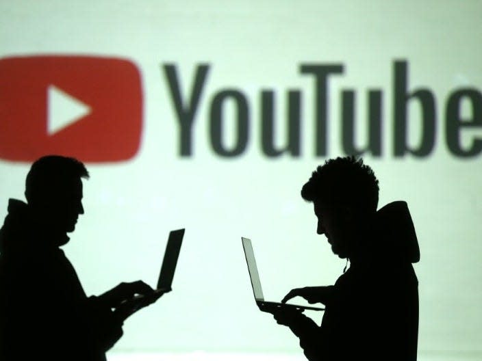 Silhouettes of mobile device users are seen next to a screen projection of Youtube logo in this picture illustration taken March 28, 2018.  REUTERS/Dado Ruvic/Illustration