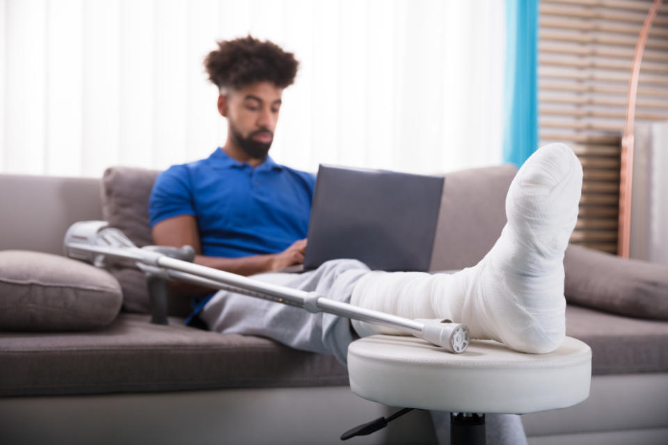 Man sitting on couch with his leg wrapped and propped up, a crutch next to him.