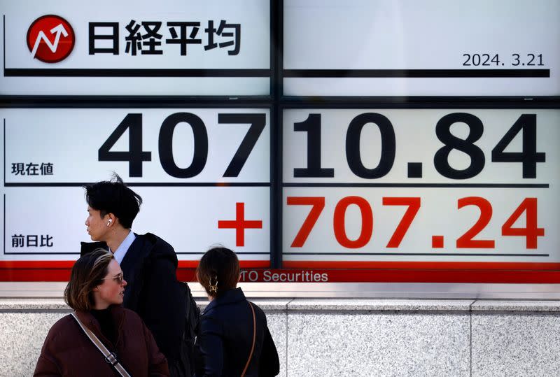 FILE PHOTO: Passersby walk in front of an electric screen displaying Japan's Nikkei share average outside a brokerage in Tokyo