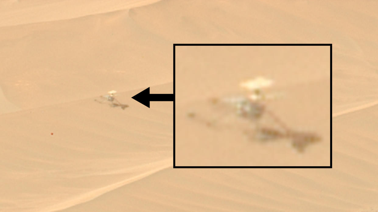  A small helicopter-like drone can be seen motionless on a reddish-orange sand dune. 