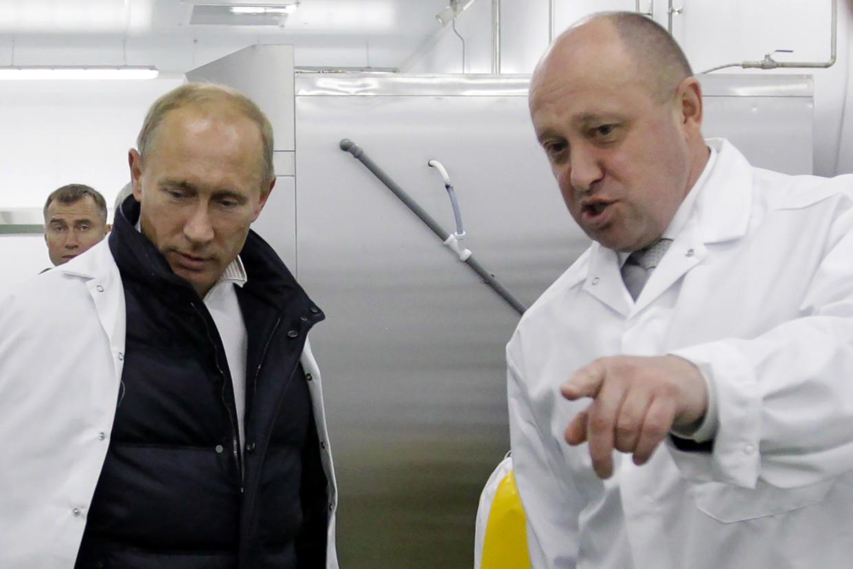 Yevgeny Prigozhin, in a commercial kitchen with Vladimir Putin, points to something out of camera range.