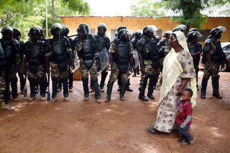 A woman walks with a child past riot police standing guard outside a polling station during a run-off presidential election in Bamako, Mali August 12, 2018. REUTERS/Luc Gnago