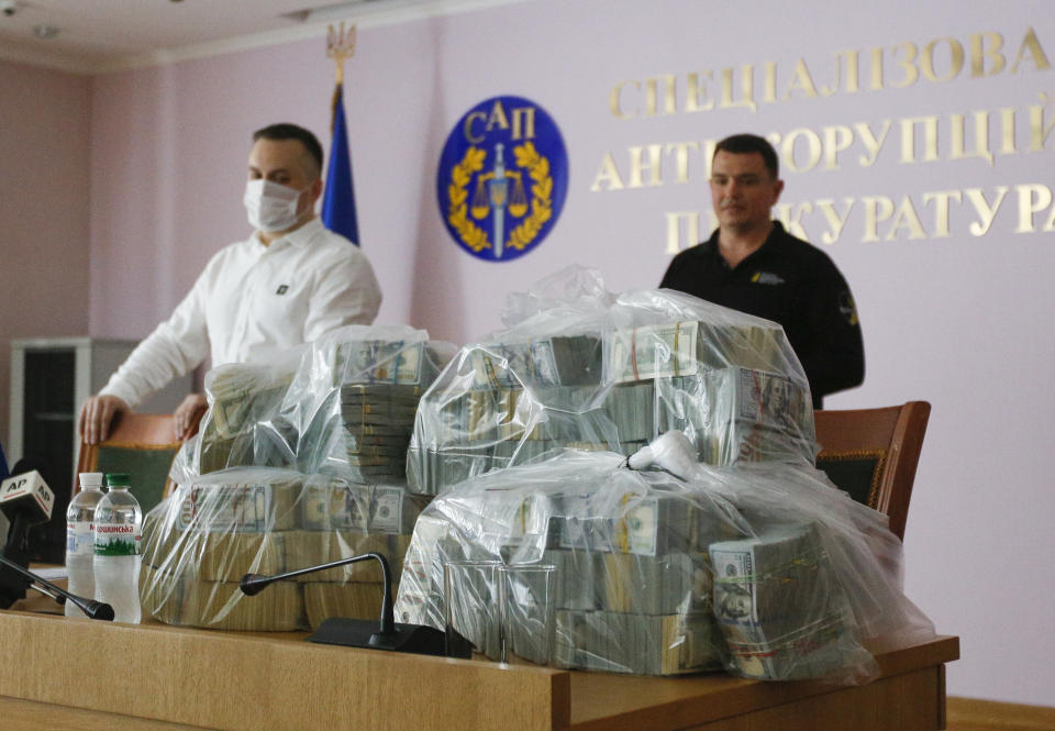 Ukraine's Anti-Corruption Prosecutor Nazar Kholodnytsky, left, and National Anti-Corruption Bureau chief Artem Sytnik at a pile of USD 6 million in plastic bags during a briefing in an anti-corruption prosecutor's office in Kyiv, Ukraine, Saturday, June 13, 2020. Ukrainian authorities say they have intercepted a USD 6 million bribe attempt at dropping a criminal investigation against the head of the Burisma natural gas company where former US Vice President Joe Biden's son once held a board seat. (AP Photo/Efrem Lukatsky)