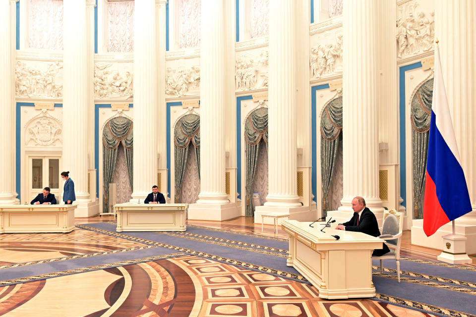 Leonid Pasechnik, head of the Luhansk People’s Republic, Denis Pushilin, head of the Donetsk People’s Republic, and Russian President Vladimir Putin sit at widely distanced desks in a large hall during a ceremony. 