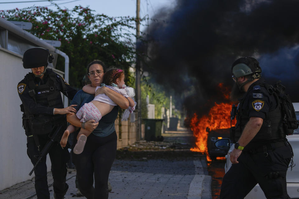 FILE - Police officers evacuate a woman and a child from a site hit by a rocket fired from the Gaza Strip, in Ashkelon, southern Israel, Saturday, Oct. 7, 2023. The rockets were fired as Hamas announced a new operation against Israel. (AP Photo/Tsafrir Abayov, File)