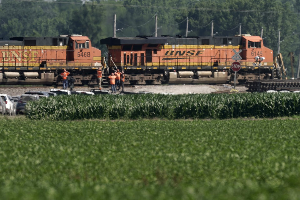 Workers watch Tuesday, June 28, 2022 as a freight train moves through the crossing where an Amtrak train derailed Monday near Mendon, Mo. The train derailed after hitting a dump truck Monday killing the truck driver and other people on the train and injuring several dozen other passengers on the Chicago-bound train. (AP Photo/Charlie Riedel)