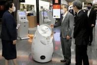 FILE - In this June 28, 2021, file photo, Japanese Prime Minister Yoshihide Suga, center, stands by a remotely-controlled guide robot at Haneda international airport in Tokyo. The pressure of hosting an Olympics during a still-active pandemic is beginning to show in Japan. Amid the criticism, Suga went to Tokyo’s Haneda international airport June 28 to inspect virus testing for arrivals. He vowed to ensure appropriate border controls as a growing number of Olympic and Paralympic athletes, officials and media begin entering Japan for the games.(Kyodo News via AP, File)
