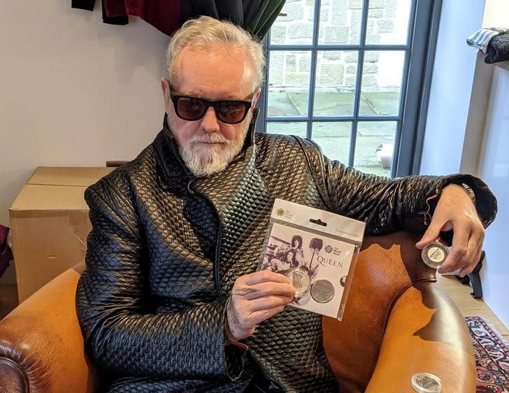 Foto del baterista de Queen, Roger Taylor, sosteniendo una moneda conmemorativa de la banda británica