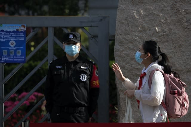 A student wearing a protective face mask to help curb the spread of the new coronavirus waves to teachers as she arrives for the reopening of a primary school in Beijing