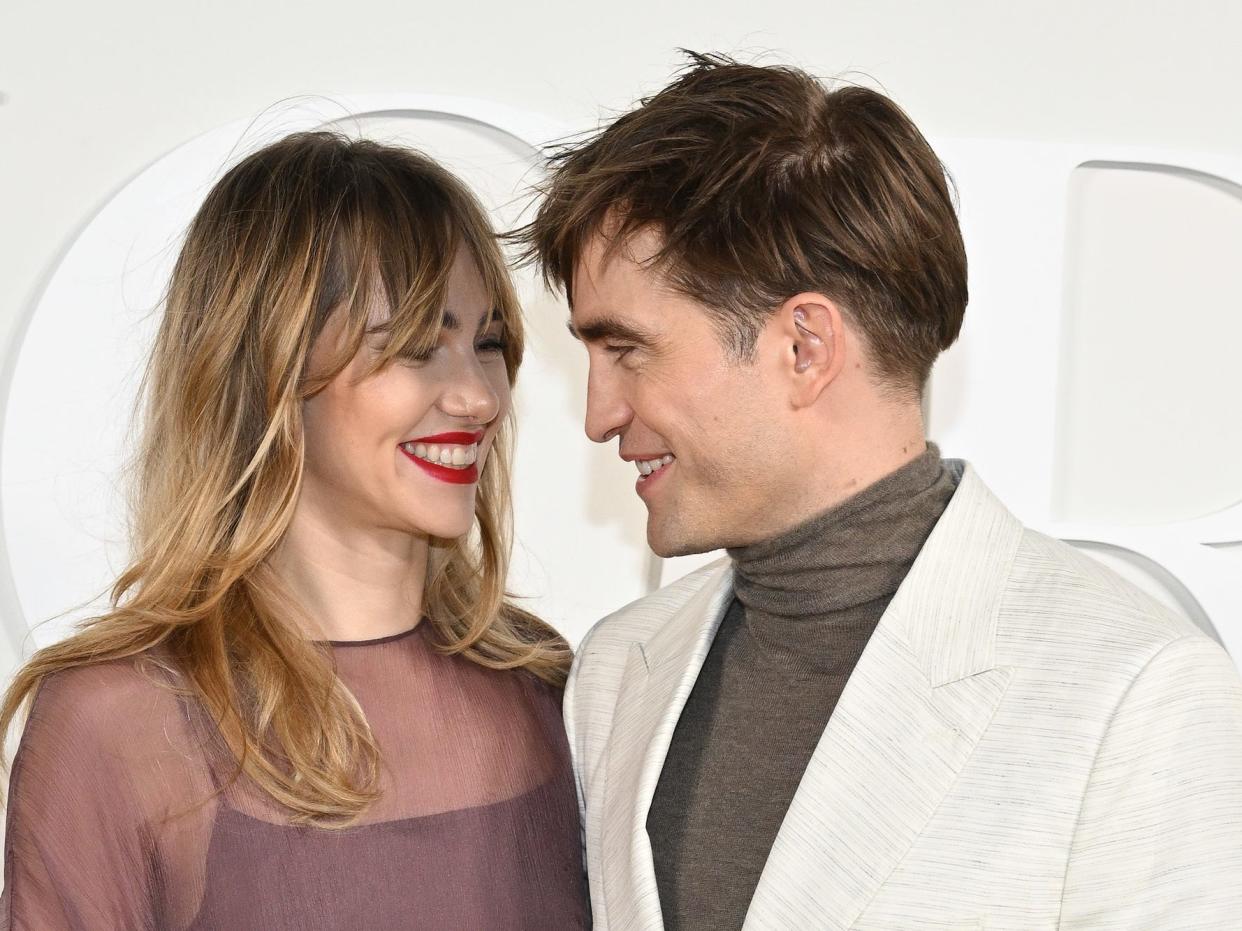 Suki Waterhouse and Robert Pattinson look at each other.