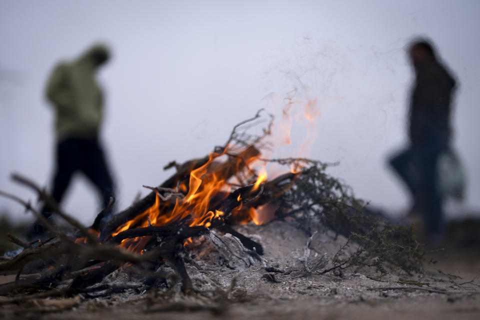 People seeking asylum keep warm near a fire as they wait to be processed, after crossing the border with Mexico nearby, Thursday, April 25, 2024, in Boulevard, Calif. Mexico has begun requiring visas for Peruvians in response to a major influx of migrants from the South American country. The move follows identical ones for Venezuelans, Ecuadorians and Brazilians, effectively eliminating the option of flying to a Mexican city near the U.S. border. (AP Photo/Gregory Bull)