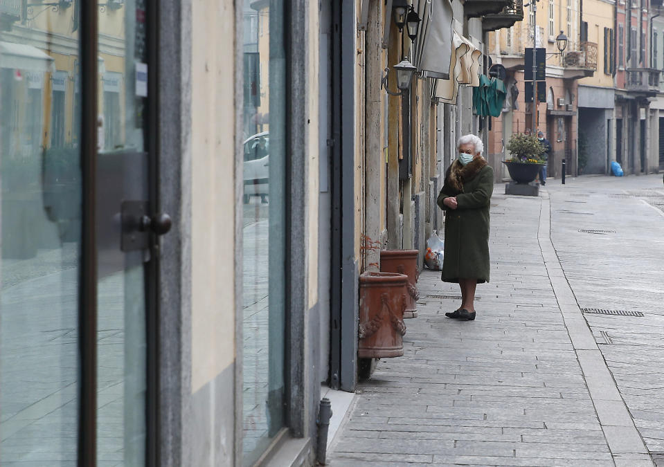 In this photo taken on Thursday, March 12, 2020, an elderly woman wearing a mask waits to enter a deli meat and cold cuts shop in Codogno, Italy. The northern Italian town that recorded Italy’s first coronavirus infection has offered a virtuous example to fellow Italians, now facing an unprecedented nationwide lockdown, that by staying home, trends can reverse. Infections of the new virus have not stopped in Codogno, which still has registered the most of any of the 10 Lombardy towns Italy’s original red zone, but they have slowed. For most people, the new coronavirus causes only mild or moderate symptoms. For some it can cause more severe illness. (AP Photo/Antonio Calanni)
