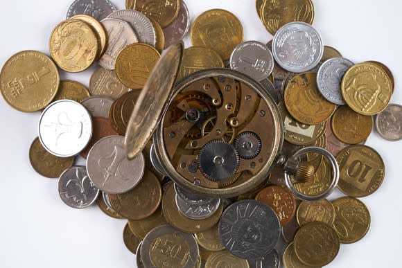 A clock with the complicated clockwork exposed, on top of a pile of coins.