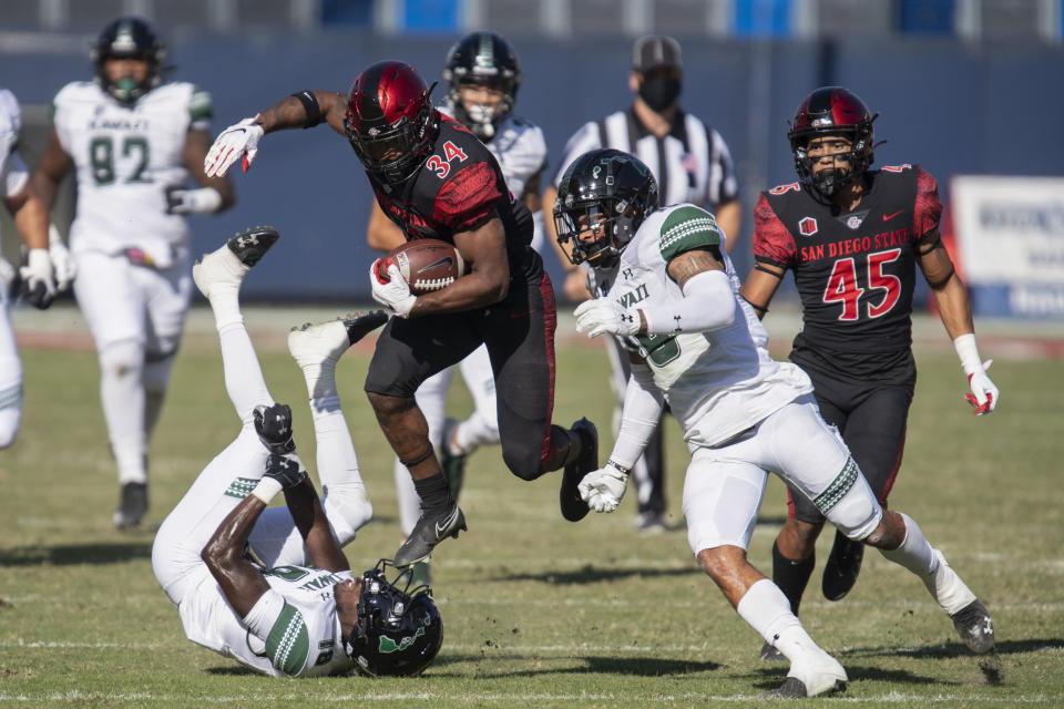 San Diego State running back Greg Bell, center, leaps over Hawaii defensive back Quentin Frazier, bottom left, during the first half of an NCAA college football game Saturday, Nov. 14, 2020, in Carson, Calif. (AP Photo/Kyusung Gong)