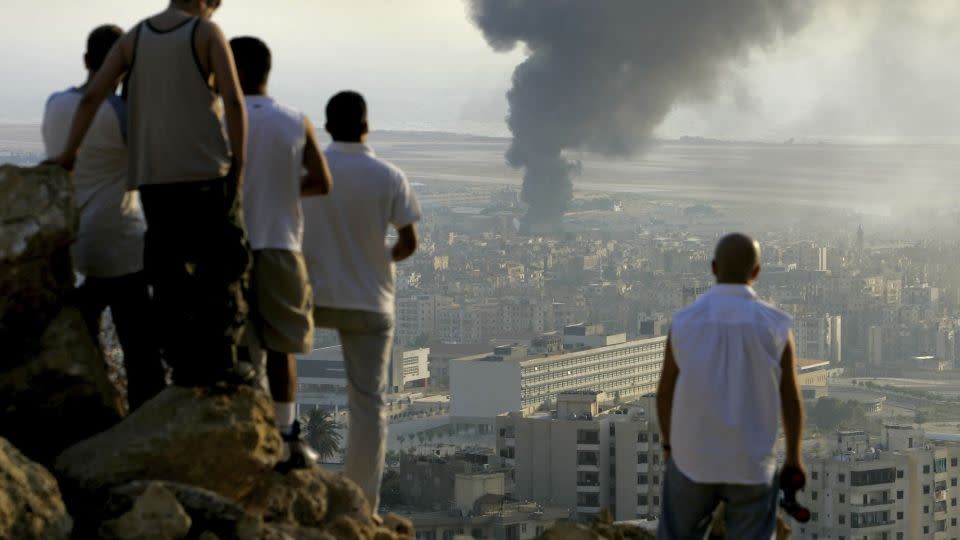 Lebanese youths gather on a hilltop overlooking the city of Beirut to watch smoke continuing to billow from a fuel dump at Beirut International Airport, which was hit by an Israeli airstrike, 2006. - Ben Curtis/AP