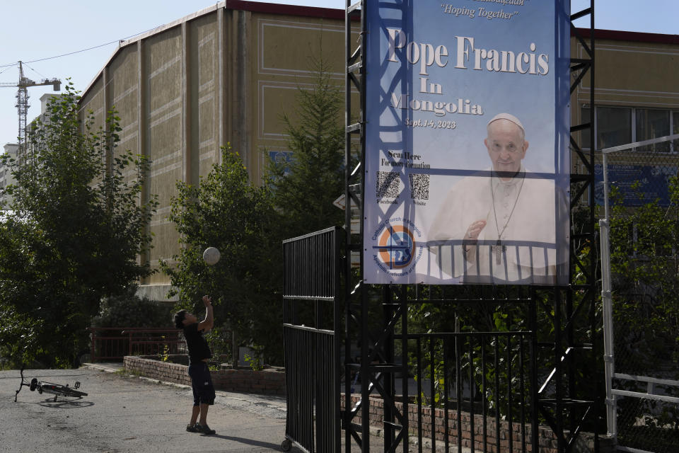 A Mongolian child plays with a ball near a banner promoting the visit of Pope Francis in Ulaanbaatar, Mongolia on Monday, Aug. 28, 2023. When Pope Francis travels to Mongolia this week, he will in some ways be completing a mission begun by the 13th century Pope Innocent IV, who dispatched emissaries east to ascertain the intentions of the rapidly expanding Mongol Empire and beseech its leaders to halt the bloodshed and convert.(AP Photo/Ng Han Guan)