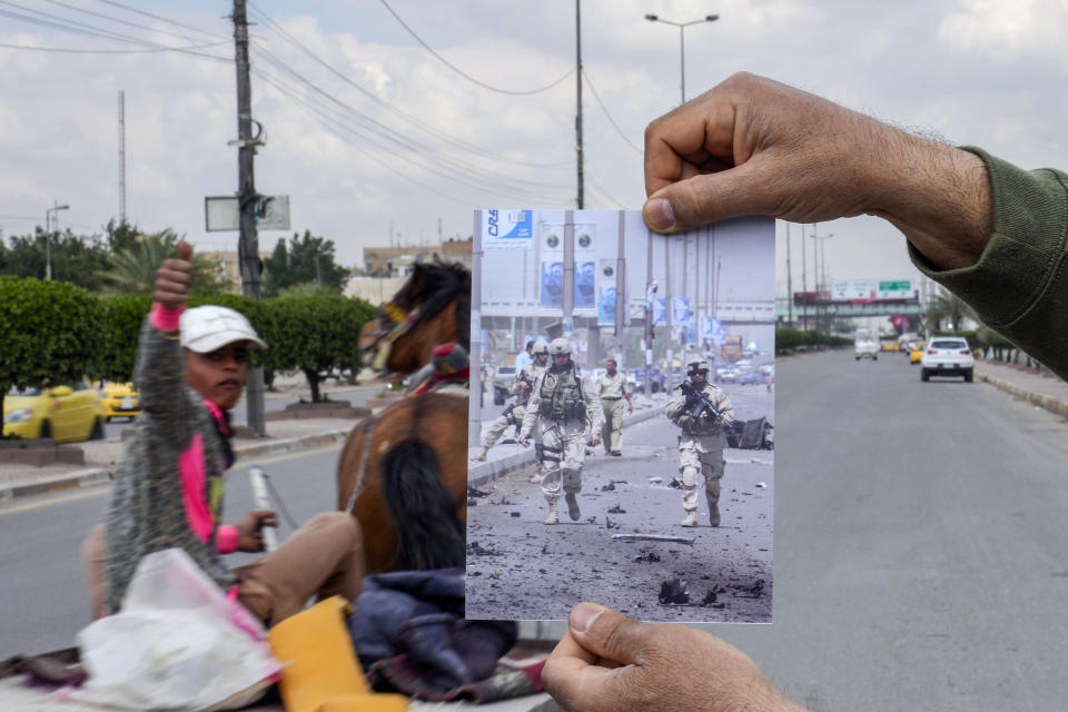 A photograph of U.S. soldiers securing the area where a car bomb exploded in the Maysalun square in Baghdad, Saturday, April 30, 2005, is inserted into the scene at the same location Tuesday, March 21, 2023, 20 years after the U.S. led invasion on Iraq and subsequent war. (AP Photo/Hadi Mizban)