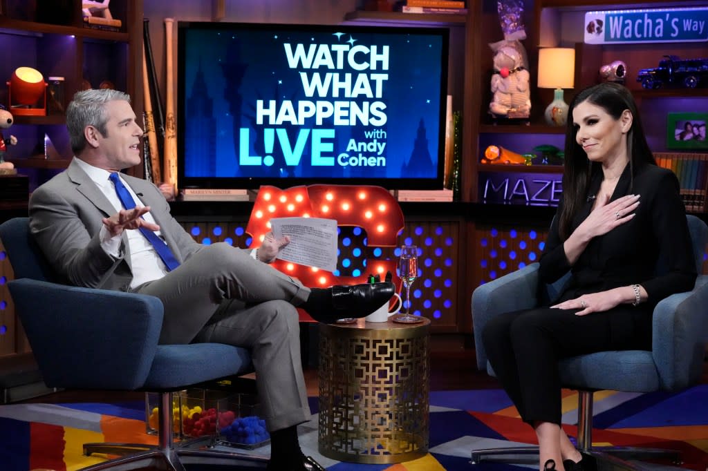 A screenshot from Watch What Happens Live where Andy Cohen is on the left in a grey suit sitting with his legs crossed, Heather Dubrow is sitting across from him in a black dress with her hand over her heart