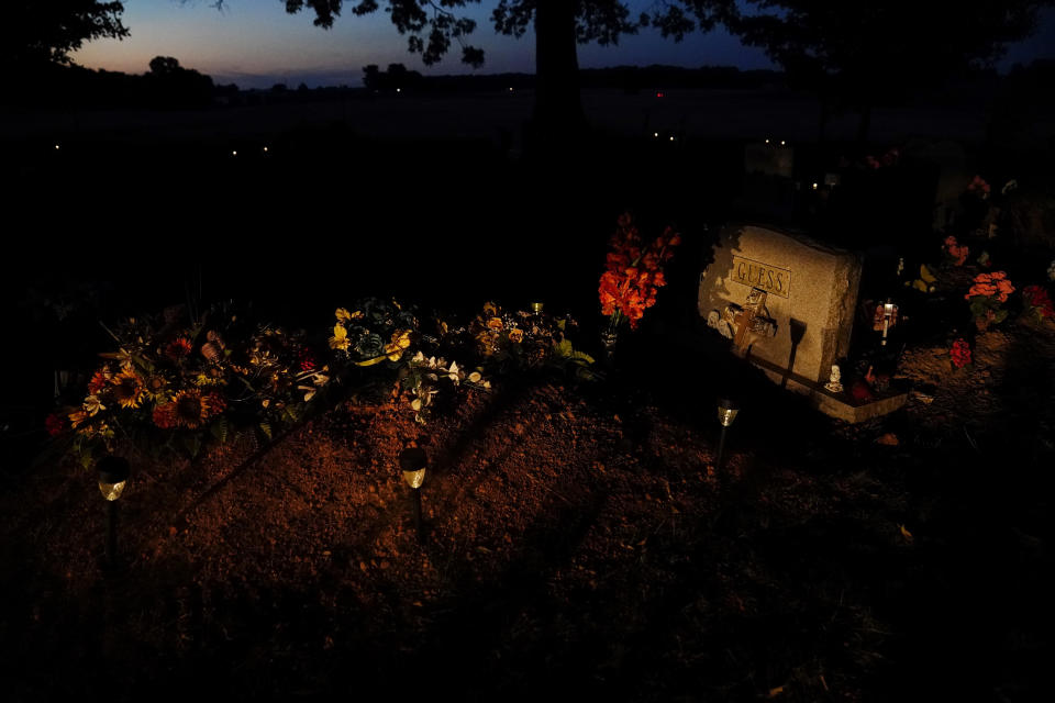 The sun sets near David Guess' grave on Thursday, June 23, 2022, in Athens, Ala. Guess, a 51-year-old small-town father of four struggled with addiction. Guess’ death began with an argument over a car part. Police say he was shot by an acquaintance and dumped in an Alabama forest near a place called Chicken Foot Mountain. (AP Photo/Brynn Anderson)