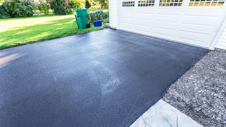 A fresh blacktop resealing job just finished on this asphalt driveway in a suburban residential district.