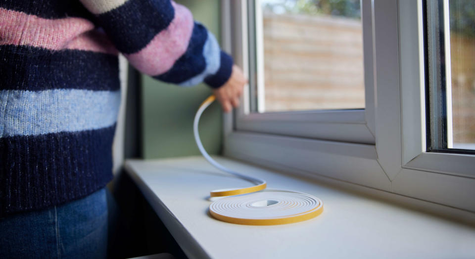 Woman draught proofing a window with plastic sealing strip