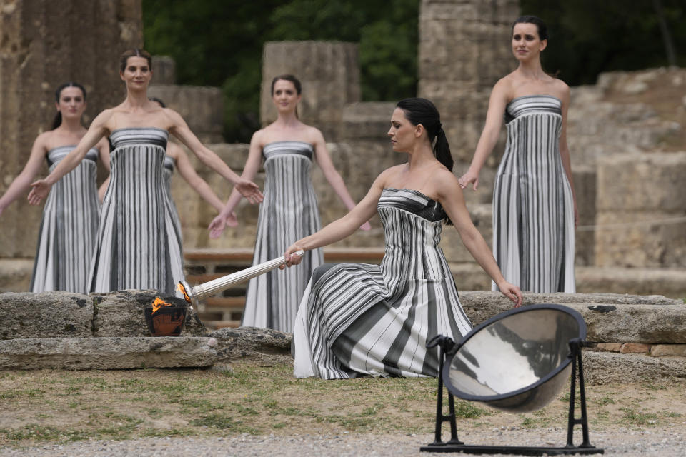 Actress Mary Mina, playing high priestess, lights a torch during the official ceremony of the flame lighting for the Paris Olympics, at the Ancient Olympia site, Greece, Tuesday, April 16, 2024. The flame will be carried through Greece for 11 days before being handed over to Paris organizers on April 26. (AP Photo/Thanassis Stavrakis)