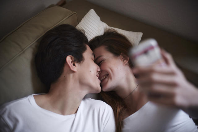 Couple lying on couch with smartphone kissing