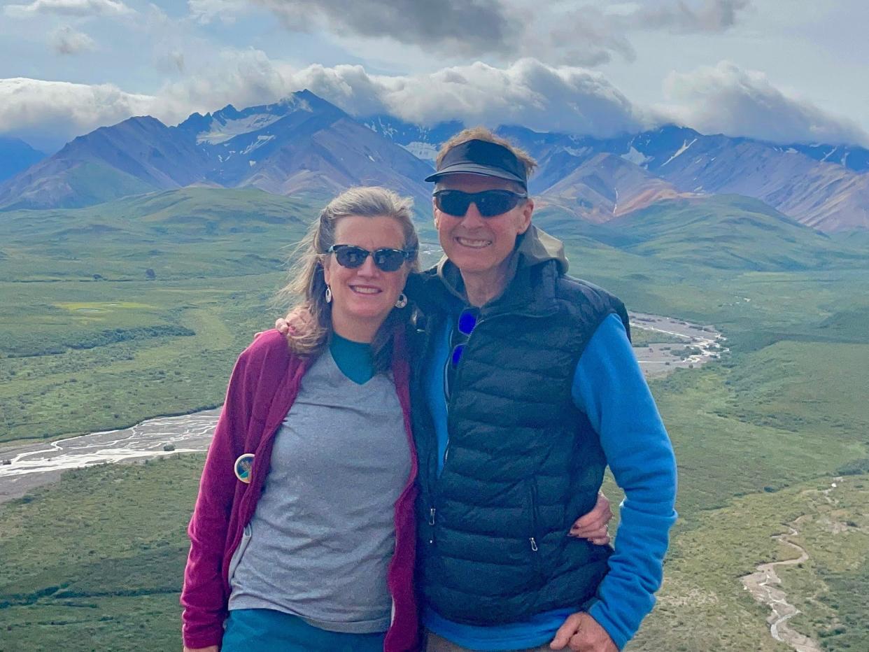 katie bausler and her husband smiling in denali national park with mountains in the background