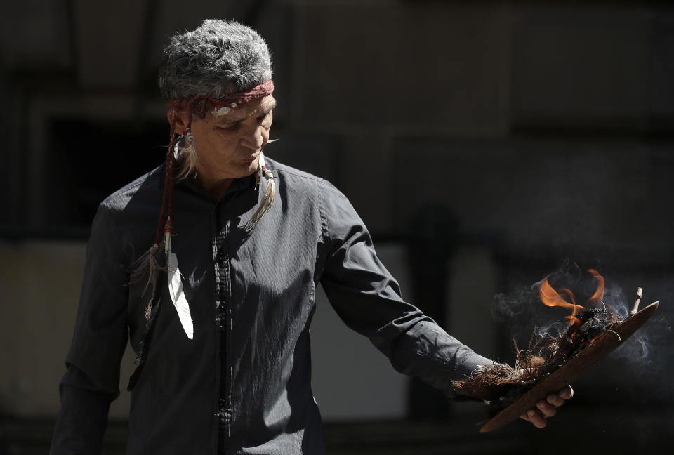 An Aboriginal man lights a fire for an indigenous ceremony as climate change protestors from the Extinction Rebellion movement gather to demonstrate at Town Hall in Sydney, Tuesday, Oct. 8, 2019. In a series of protests also including Australian cities of Melbourne, Brisbane and Perth, protestors are demanding much more urgent action against climate change. (AP Photo/Rick Rycroft)