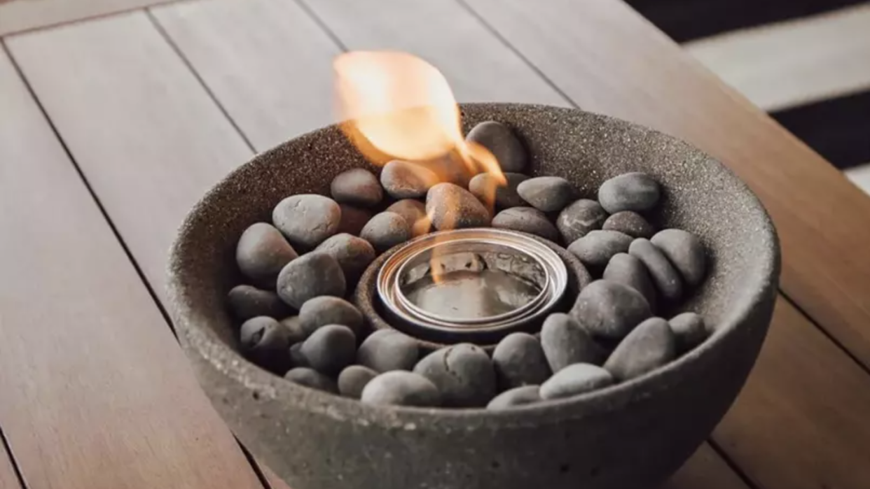 gray stone bowl filled with dark gray stones and a flames coming from the middle