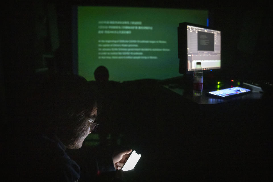 A production crew member looks at his cellphone as the documentary film "Wuhan, I Am Here" plays in a screening room in Beijing, Saturday, Jan. 15, 2022. The homeless, the sick, the elderly: For people who fell through the cracks of the official system, the then-unprecedented decision to isolate the central Chinese city of Wuhan and its 13 million people was a matter of life or death. Director Lan Bo hopes to sound the alarm with a documentary about volunteers who helped neighbors get food and medical care following the lockdown in early 2020 of the city where the coronavirus pandemic began. (AP Photo/Mark Schiefelbein)