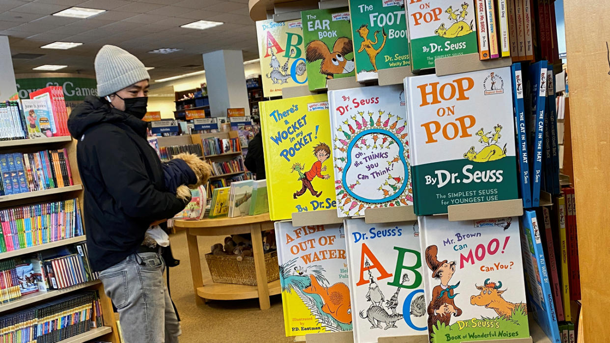 A customer in a bookstore looks at a full stand of books by Dr. Seuss, including Hop on Pop, Dr. Seuss's ABC, There's a Wocket in My Pocket, A Fish Out of Water and so on. 