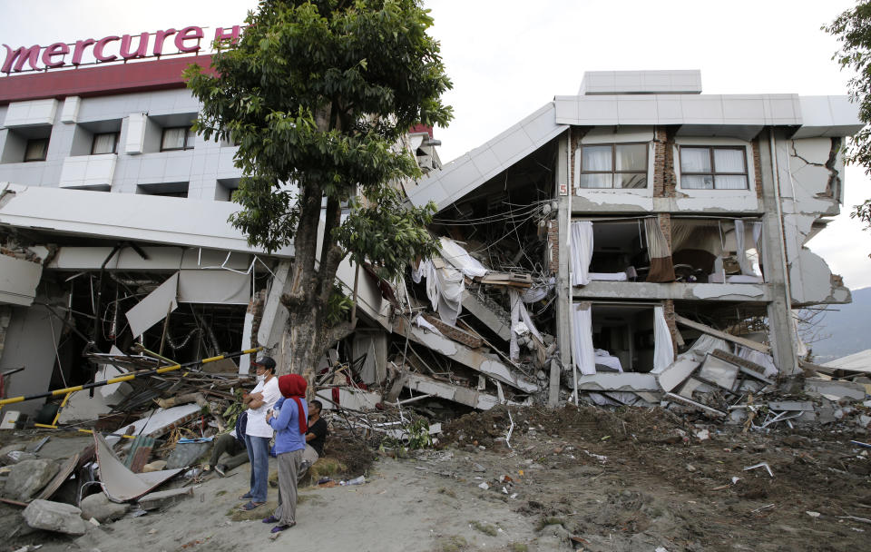 Filipinos stand beside the heavily damaged Mercure hotel after a massive earthquake and tsunami hit Palu, Central Sulawesi, Indonesia Thursday, Oct. 4, 2018. Life is on hold for thousands living in tents and shelters in the Indonesian city hit by a powerful earthquake and tsunami, unsure when they'll be able to rebuild and spending hours each day often futilely trying to secure necessities such as fuel for generators. (AP Photo/Aaron Favila)