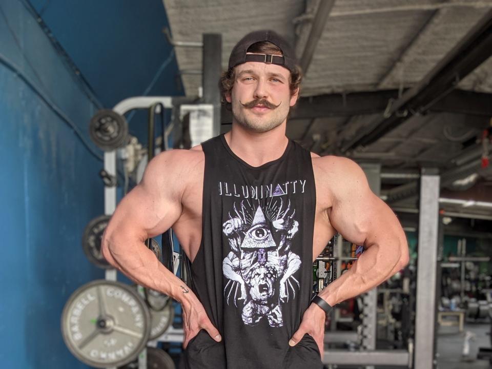 Muscled bodybuilder Carter Kissick, wearing a baseball cap and tank top, poses in a gym.