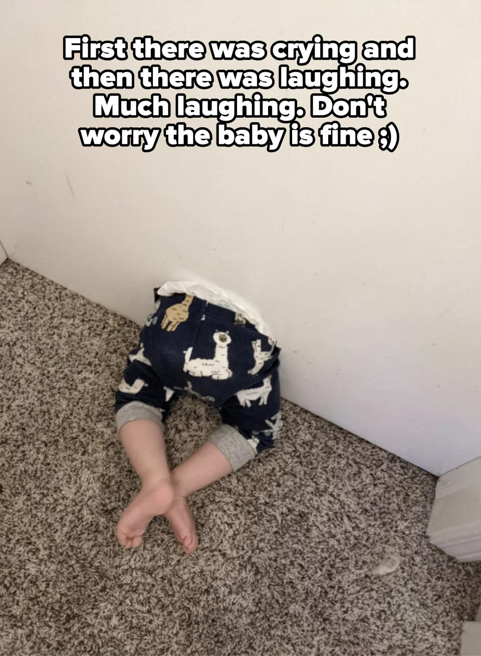 A baby wearing animal print pants and a white shirt is head down, with only legs visible, stuck in the corner against a wall and carpeted floor