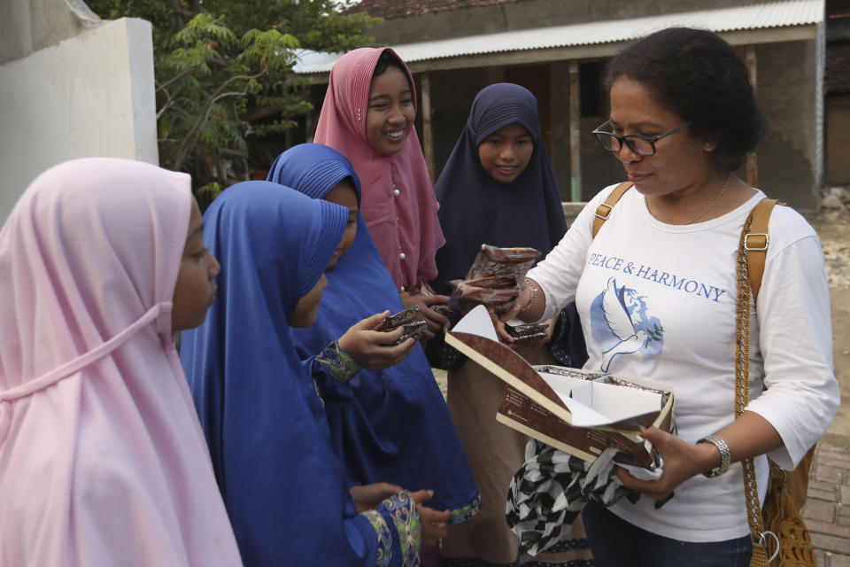 Ni Luh Erniati, right, gives cakes to Ali Fauzi's daughter and relatives while visiting Fauzi's home in Tenggulun, East Java, Indonesia, on Saturday, April 27, 2019. Erniati, whose husband was killed in the 2002 Bali bombings, and Fauzi, a former bombmaker whose brothers helped orchestrate the Bali attack, have reconciled as part of a peacebuilding program bringing together ex-terrorists and victims. (AP Photo/Tatan Syuflana)