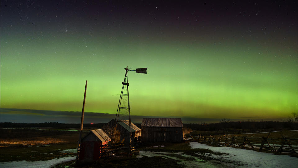  Green band of aurora light in the sky above a rural building. 