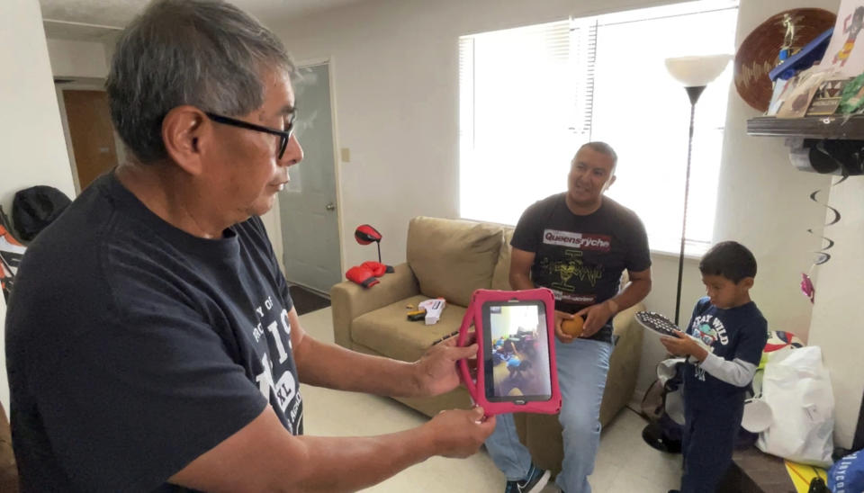Myron Ami shows a video of his daughter singing to his grandson, Micca, right, when he was a baby while visiting the home where Micca lives with his father, Darryl Madalena, center, at Jemez Pueblo, N.M., Oct. 7, 2022. Micca's mother died after getting a growth removed from her liver. Getting on a transplant list was never discussed. (AP Photo/Susan Montoya Bryan)