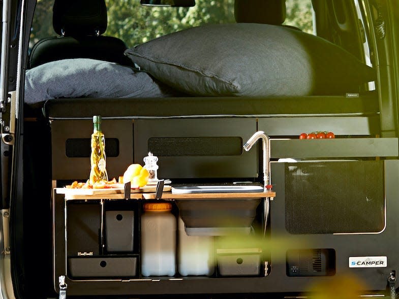 The trunk of the EQV open revealing a mini kitchen. The van is parked among trees.