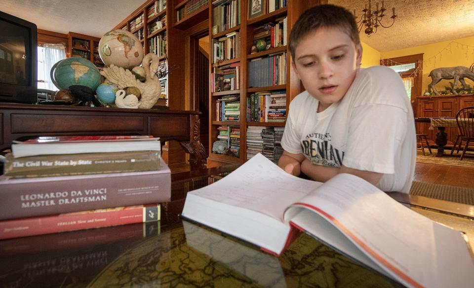 Tyler Spangler, age 12, looks at the course book his mother bought for a Penn State York calculus with analytic geometry class he starts in a few weeks. Behind him are just a few of the globes he has collected because he loves traveling and geography.