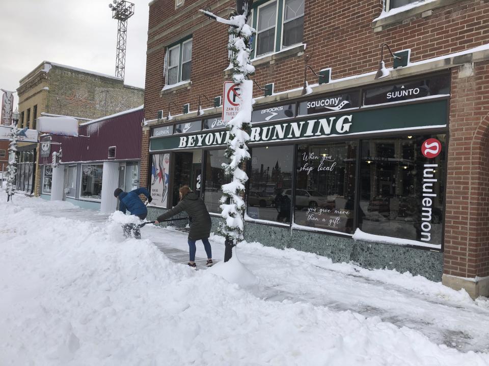 Jake Olson, left, and Mackenzie Weinberger shovel snow outside of a store in downtown Fargo, N.D. on Monday, Dec. 30, 2019, following a blizzard that dropped over a foot of snow in the area and closed streets, highways and many businesses. Fargo Mayor Tim Mahoney said the storm was one of the worst he's seen because it began with a sheet of ice and ended with 40 mph wind gusts. Mahoney asked residents to be patient and help their neighbors. (AP Photo/Dave Kolpack)