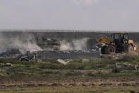 An Israeli tank secures while bulldozer demolishes the remains of Karni commercial border crossing between Israel and Gaza Strip, east of Gaza City, Tuesday, Dec. 6, 2022. Israeli bulldozers and cranes were seen Tuesday dismantling a commercial crossing point on the eastern side of Gaza City as Israel decided to extend a security barrier at the location of the long-defunct terminal. (AP Photo/Adel Hana)