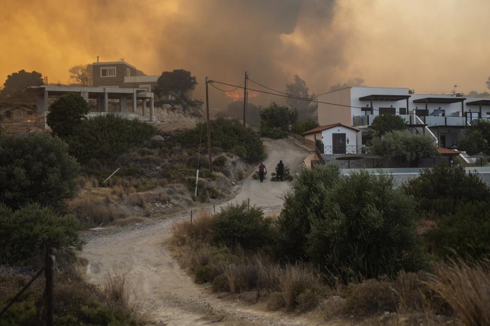 Locals pull tree branches as a wildfire burns in Gennadi village, on the Aegean Sea island of Rhodes, southeastern Greece, on Tuesday, July 25, 2023. A firefighting plane has crashed in southern Greece, killing both crew members, as authorities are battling fires across the country amid a return of heat wave temperatures. (AP Photo/Petros Giannakouris)