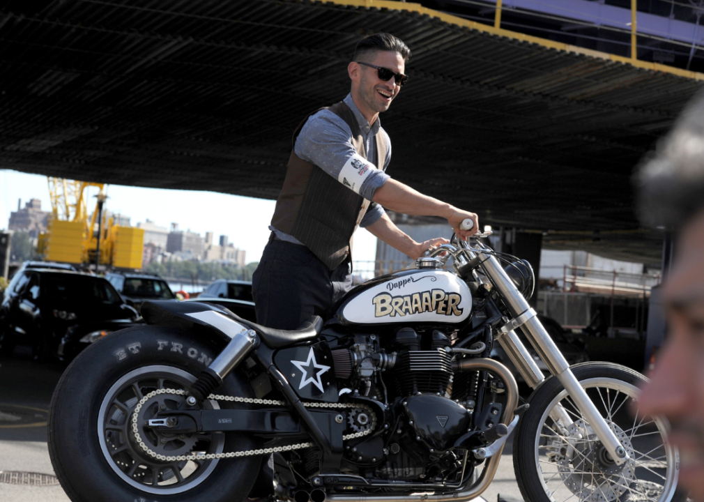 A man smiling while holding up a motorcycle in New York.