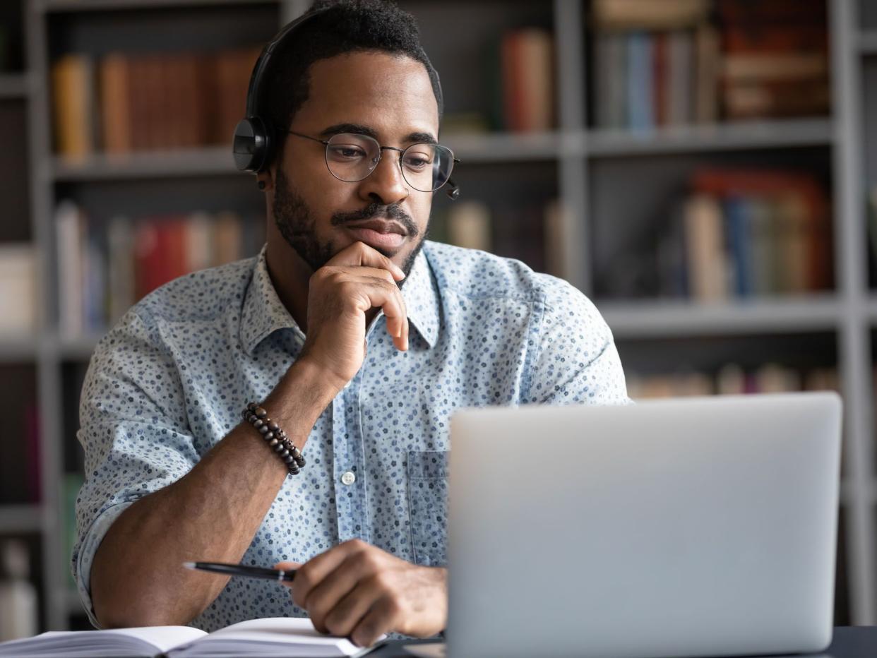 Focused African man wear headphones with microphone looking at laptop screen listens audio lesson learn foreign language with tutor makes video call. Student watching webinar, e study on-line concept