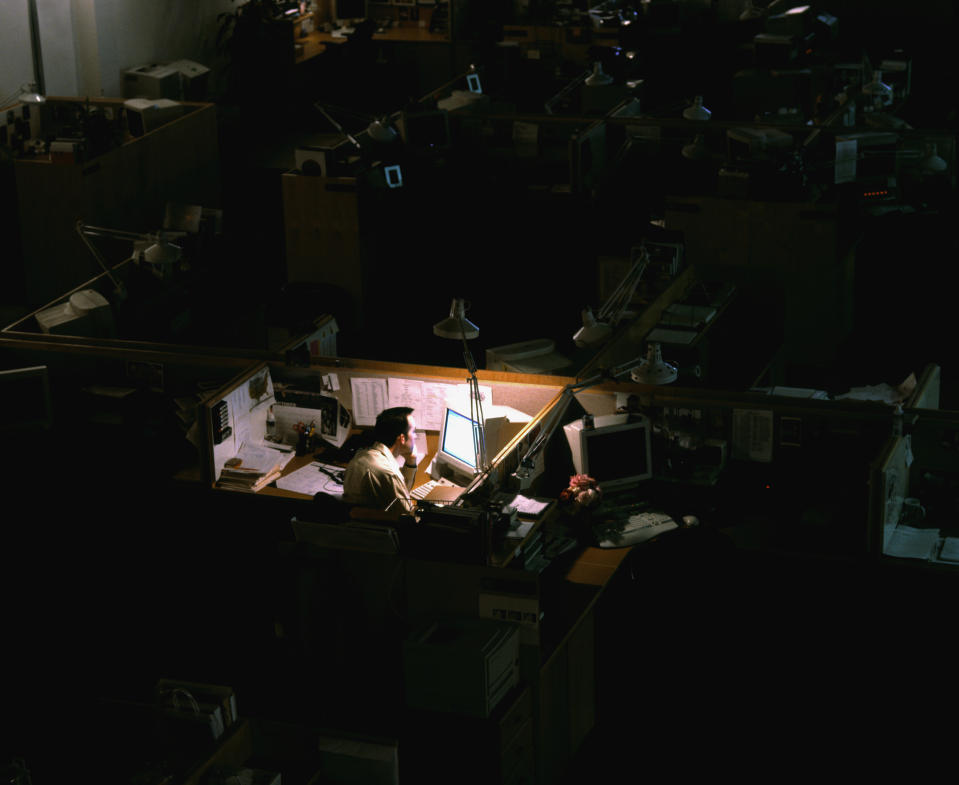 Person working late in an office with dim lighting, surrounded by desks and computers