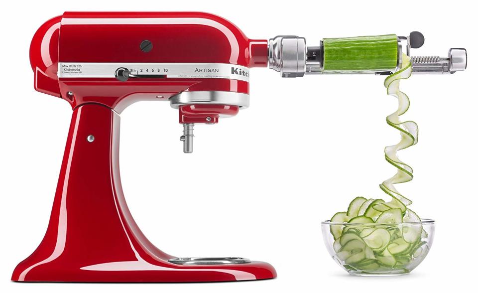 a red kitchenaid mixer with a spiralizer attachment on the front cutting cup a cucumber